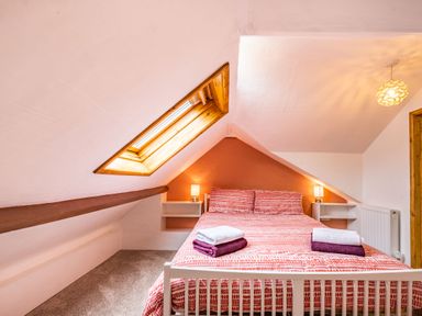 A bedroom with a double bed under a sloping ceiling with a skylight window and bedside tables with lamps at Pendre Cottage in Cenarth