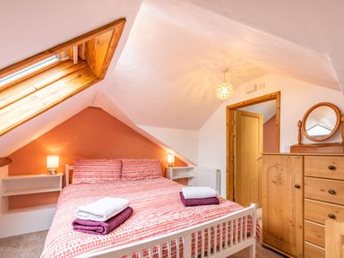 A bedroom with a double bed with folded towels bedside tables with lamps a wooden dresser and a skylight window at Pendre Cottage in Cenarth