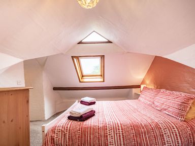 A bedroom with a bed covered in red and white patterned bedding towels on the bed a skylight window and a wooden dresser at Pendre Cottage in Cenarth