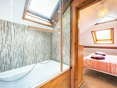A bathroom with a bathtub and shower next to a bedroom with a bed and towels at Pendre Cottage in Cenarth