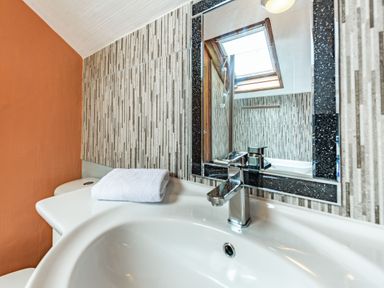 A bathroom sink with a folded white towel on the counter and a mirror reflecting a skylight at Pendre Cottage in Cenarth