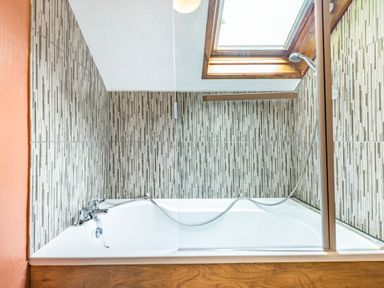A bathtub with showerhead and tiled walls under a skylight at Pendre Cottage in Cenarth
