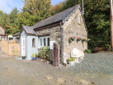 A stone cottage with a white door and window surrounded by plants and a bench outside at Pendre Cottage in Cenarth