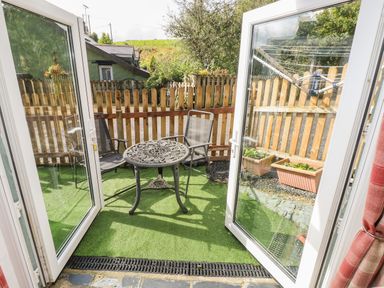 A small outdoor patio with two chairs and a round metal table surrounded by a wooden fence at Pendre Cottage in Cenarth