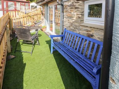 An outdoor patio area with a blue wooden bench a metal table and chair set on artificial grass at Pendre Cottage in Cenarth