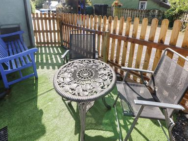 A small outdoor patio area with a metal table, two mesh chairs, a wooden bench, and a wooden fence at Pendre Cottage in Cenarth