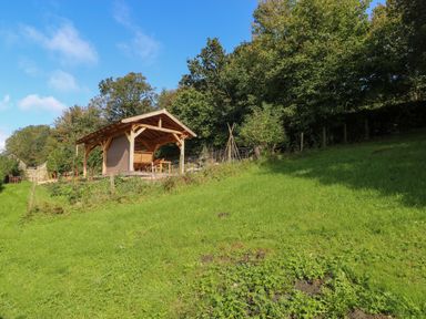 A wooden shelter with a table and chairs on a grassy hillside near trees and fencing at Pendre Cottage in Cenarth