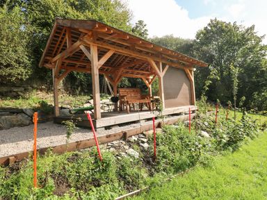 An outdoor wooden gazebo with a bench and a grill in a garden area at Pendre Cottage in Cenarth
