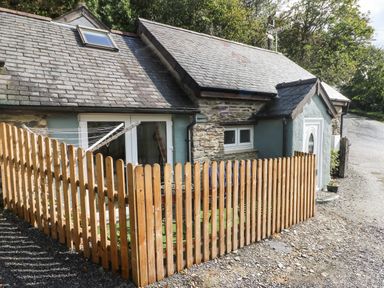 A stone cottage with a wooden picket fence and gravel driveway at Pendre Cottage in Cenarth