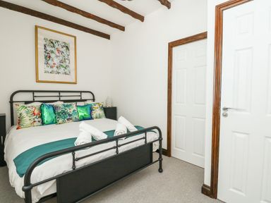 A bedroom with a black metal bed frame pillows with tropical prints white doors and wooden ceiling beams at The Brewery in Brewers Quay Harbour