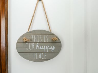 A hanging wooden sign with the words This is our happy place on a white wall