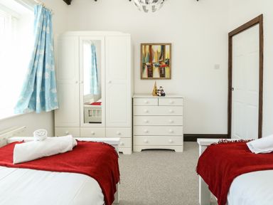 A bedroom with two single beds with red blankets a white wardrobe a white chest of drawers and blue curtains at The Brewery in Brewers Quay Harbour