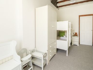 A bedroom with white bunk beds wardrobe small table chairs and a bedside table with a teddy bear at The Brewery in Brewers Quay Harbour