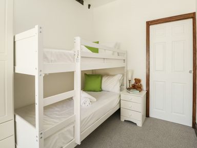 A bedroom with white bunk beds green pillows a white bedside table with a lamp a teddy bear and books at The Brewery in Brewers Quay Harbour