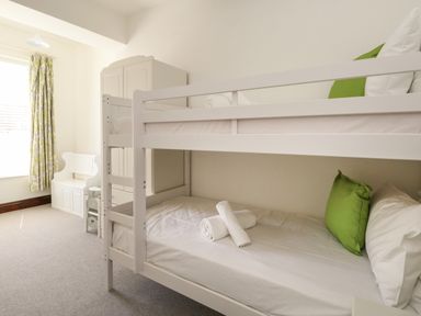A bedroom with a white bunk bed green pillows white towels a white wardrobe and a white bench near a window with green patterned curtains at The Brewery in Brewers Quay Harbour
