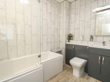 A bathroom with a bathtub glass screen toilet grey cabinets and a mirror at The Brewery in Brewers Quay Harbour