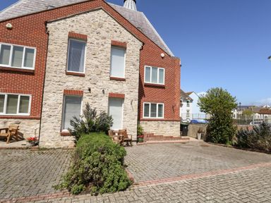 A brick and stone house with windows and a paved driveway with shrubs and outdoor chairs at The Brewery in Brewers Quay Harbour