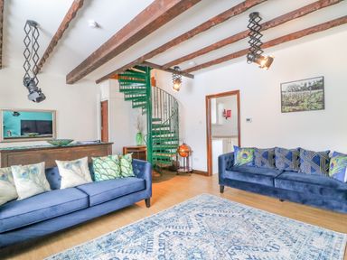A living room with two blue sofas with cushions a blue patterned rug wooden beams on the ceiling a green spiral staircase and a doorway at The Brewery Brewers Quay Harbour