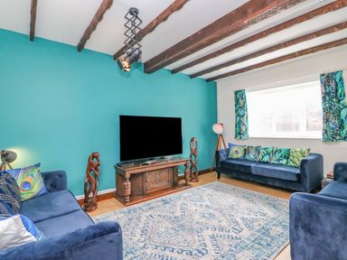 A living room with blue sofas a large patterned rug a wooden tv stand a flat screen tv and wooden ceiling beams at The Brewery in Brewers Quay Harbour