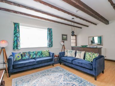 A living room with two blue sofas and patterned cushions with exposed wooden beams on the ceiling at The Brewery in Brewers Quay Harbour
