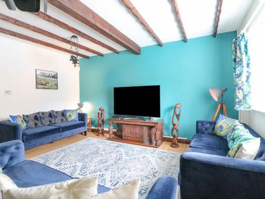 A living room with blue sofas a wooden TV stand a large flat screen TV and decorative wooden sculptures at The Brewery in Brewers Quay Harbour