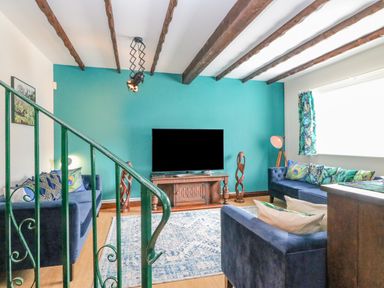 A living room with blue sofas a wooden TV stand and a teal accent wall at The Brewery in Brewers Quay Harbour