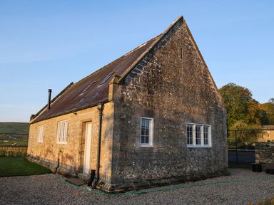 A stone building with a pitched roof and several windows on a gravel and grassy area at Greystead Institute in Bellingham
