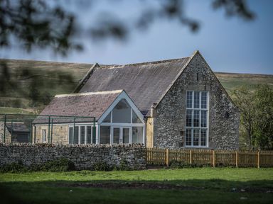 A stone building with large windows and a fenced yard in a rural area at Greystead Institute in Bellingham