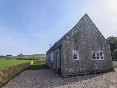 Stone building with white windows next to a gravel area and fenced grass field at Greystead Institute in Bellingham
