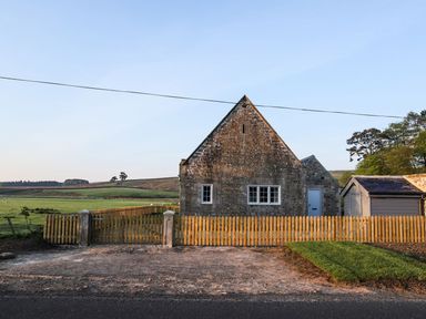 Stone house with wooden fence and gate near open grass fields at Greystead Institute in Bellingham