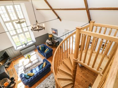 A living room with wooden spiral staircase two blue sofas and large window at Greystead Institute in Bellingham
