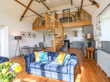 A living room with blue sofas yellow and blue cushions wooden spiral staircase and kitchen at Greystead Institute in Bellingham