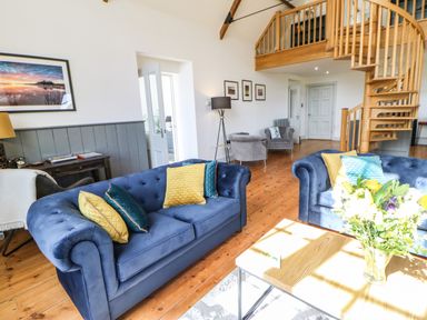 A living room with blue sofas yellow and blue cushions wooden spiral staircase and flowers on a table at Greystead Institute in Bellingham