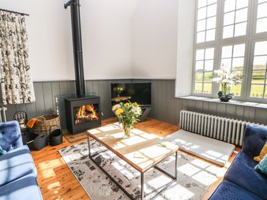 A living room with a wood stove, blue sofas, coffee table with flowers, and large windows at Greystead Institute in Bellingham