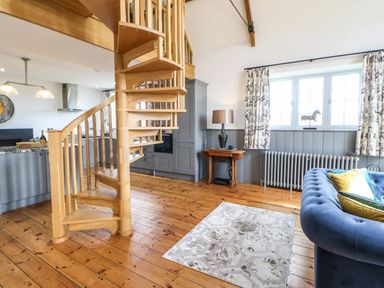 A living area with a wooden spiral staircase kitchen cabinets a rug a blue sofa and a window with curtains at Greystead Institute in Bellingham