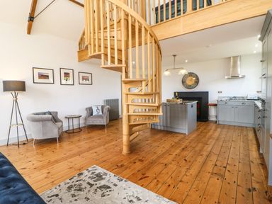 An open-plan living area with wooden spiral staircase grey kitchen cabinets and two armchairs at Greystead Institute in Bellingham