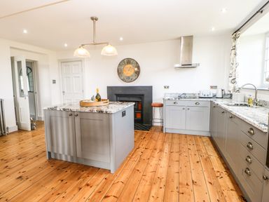 A kitchen with gray cabinets wooden floor a central island a wall clock and a stool at Greystead Institute in Bellingham