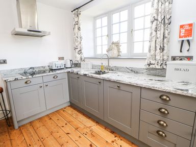 A kitchen with grey cabinets a marble countertop a window with patterned curtains and wooden flooring at Greystead Institute in Bellingham