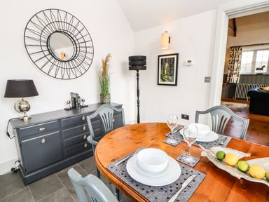 A dining area with a round wooden table set with plates and glasses and a gray sideboard with a lamp and mirror at Greystead Institute Bellingham