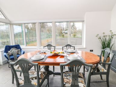 A dining table with six chairs set with bowls and glasses near large windows and a blue armchair at Greystead Institute in Bellingham