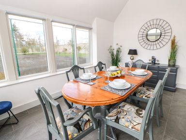 A dining room with a wooden table set for four surrounded by chairs with patterned cushions a sideboard with a lamp plants and a round mirror on the wall at Greystead Institute in Bellingham