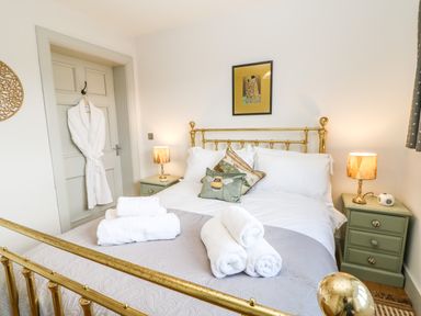 A bedroom with a brass bed frame white bedding rolled towels two bedside tables with lamps and a white robe hanging on a door at Greystead Institute in Bellingham