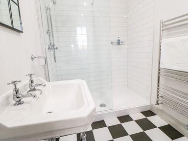 A bathroom with a white sink with two taps a walk-in shower with white tiled walls and a chrome towel rack with a white towel at Greystead Institute in Bellingham