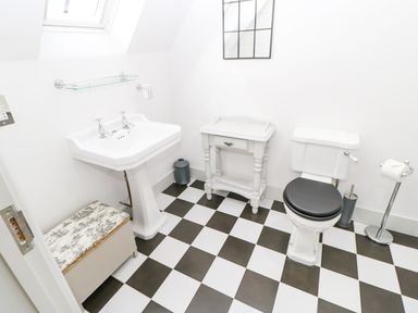 A bathroom with a pedestal sink a toilet with a black seat a small table and a cushioned storage bench at Greystead Institute in Bellingham