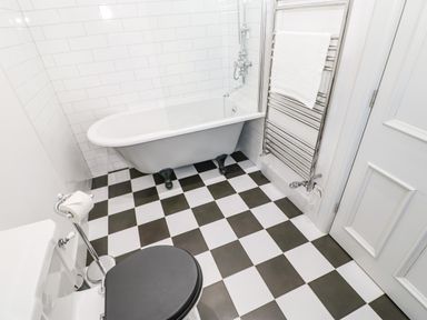 A bathroom with a black and white checkered floor a white bathtub with black feet a white toilet with a black seat a silver towel rack with a white towel and white tiled walls at Greystead Institute in Bellingham