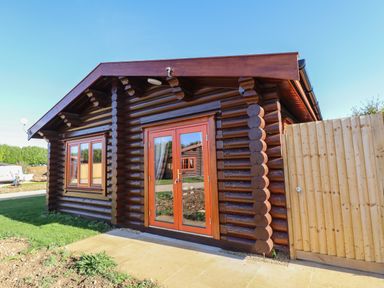 An exterior view of a small log cabin with wooden double doors and a window next to a wooden fence at Rowan Lodge in Greetham Rutland
