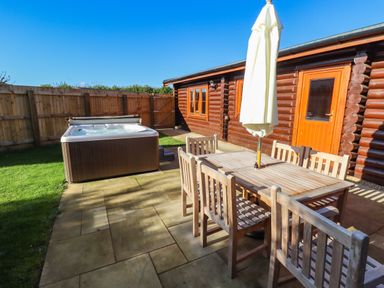 An outdoor patio area with wooden dining table and chairs a hot tub and a wooden cabin at Rowan Lodge in Greetham Rutland