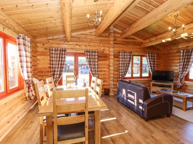 A wooden dining table with chairs and a living area with a sofa and television in a log cabin at Rowan Lodge in Greetham Rutland