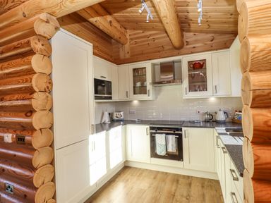 A kitchen with white cabinets and black countertop in a wooden log cabin at Rowan Lodge in Greetham Rutland