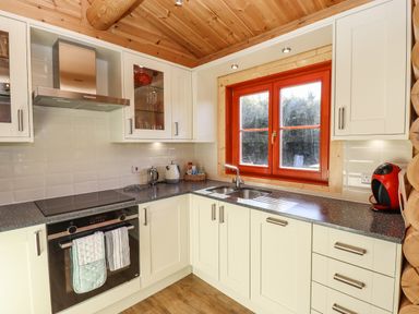A kitchen with white cabinets a black countertop a built in oven a sink under a window and a red coffee machine at Rowan Lodge in Greetham Rutland